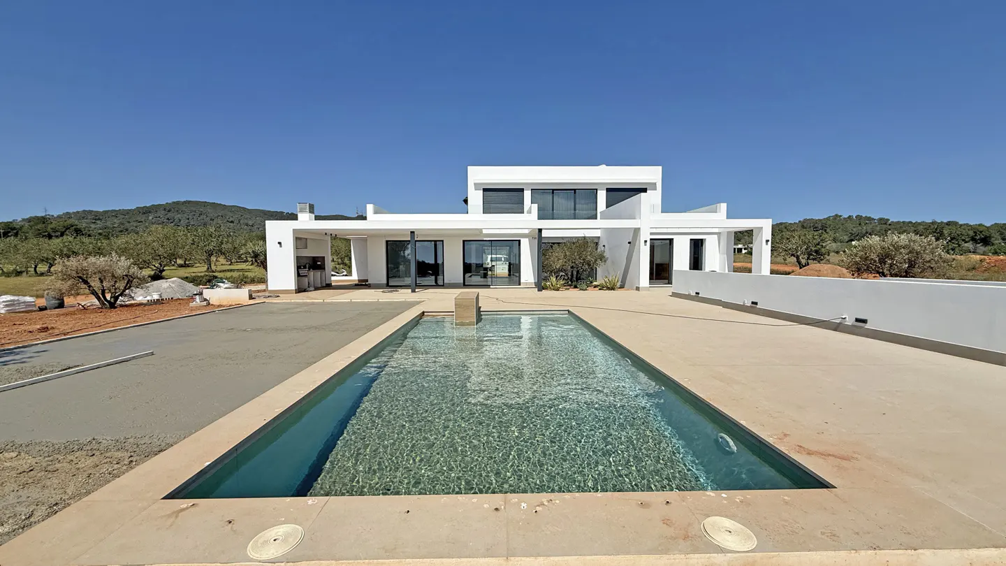 Modern white house with a rectangular pool in the foreground under a clear blue sky.