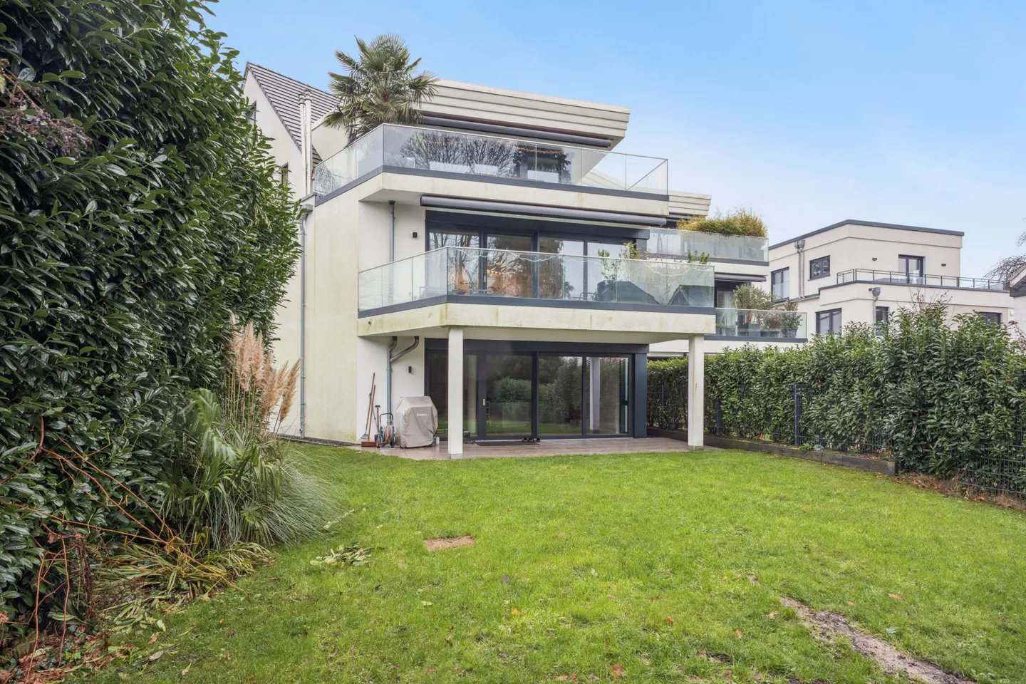 Back view of a modern three-story house with balconies and a green lawn.