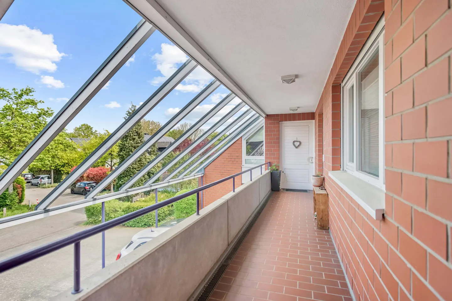 Enclosed balcony with brick wall, red tile floor, and glass roof. A white door with a heart decoration is visible at the end.