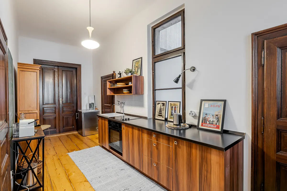 A kitchen with wood cabinets, black countertops, and wood floors. A window is above the counter, and a rug is on the floor.