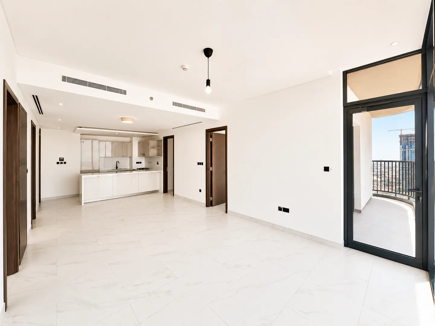 Bright, empty apartment with white walls, marble floors, and a modern kitchen. A black-framed door leads to a balcony with a city view.