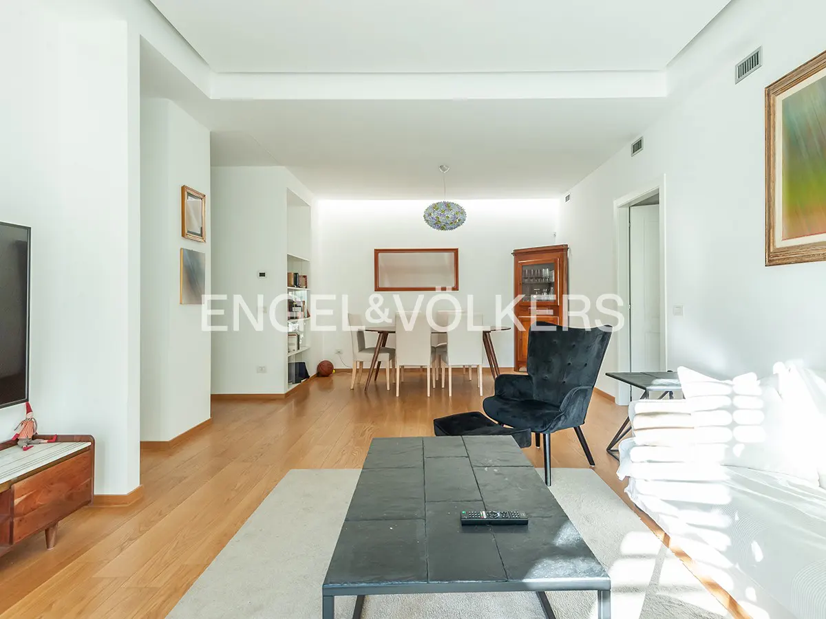 Bright living room with hardwood floors, a black coffee table, a black armchair, and a dining area in the background.