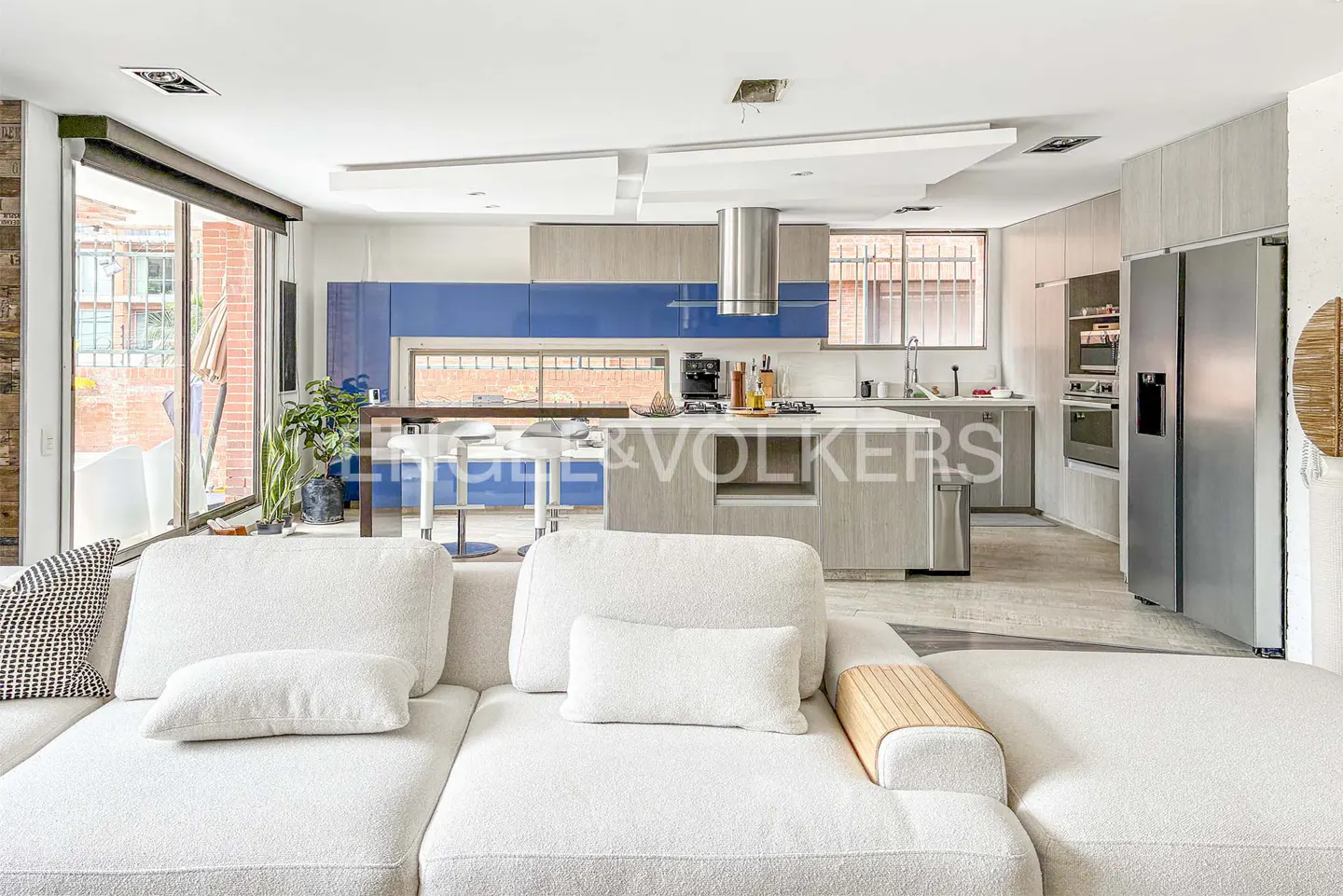 Open concept living space with a white sectional sofa in the foreground and a modern kitchen with blue cabinets in the background.