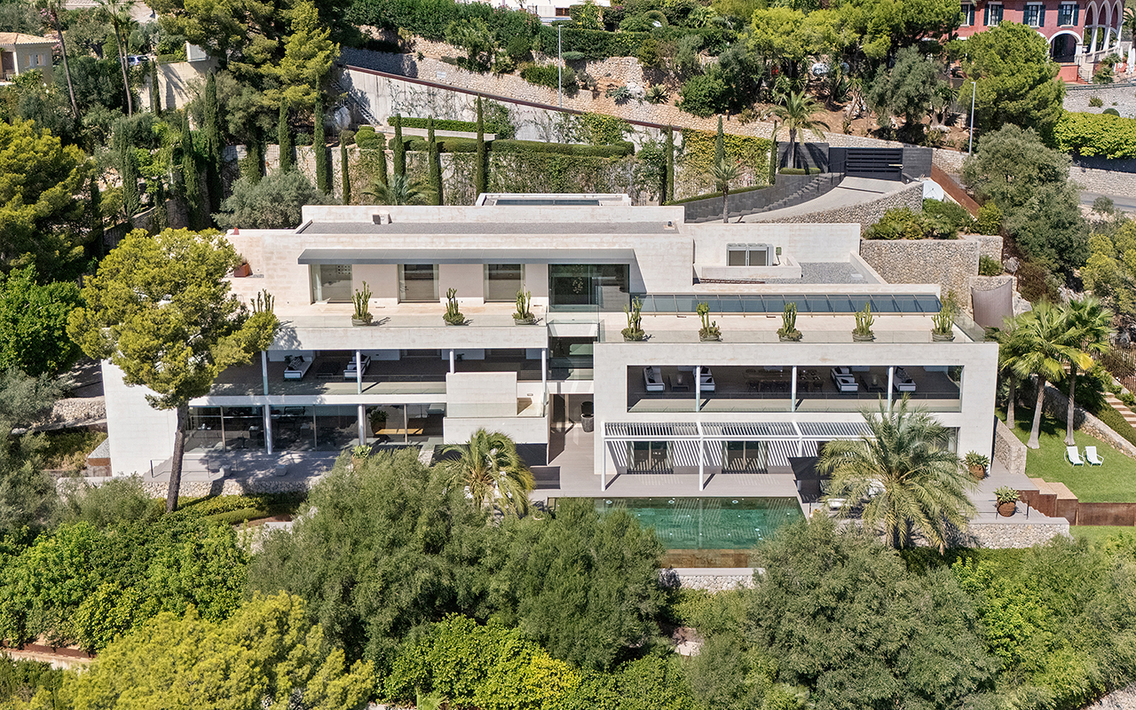 Aerial view of a modern, multi-level beige villa with a swimming pool, balconies, and lush green landscaping. [AI-generated text]