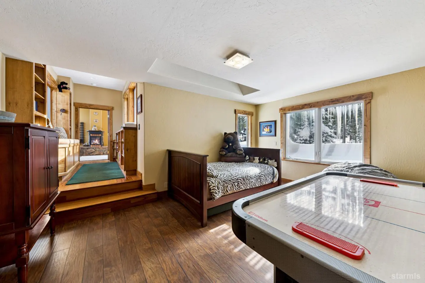 Bedroom with hardwood floors, a twin bed with a zebra-print comforter, and an air hockey table. A window shows a snowy outdoor scene.