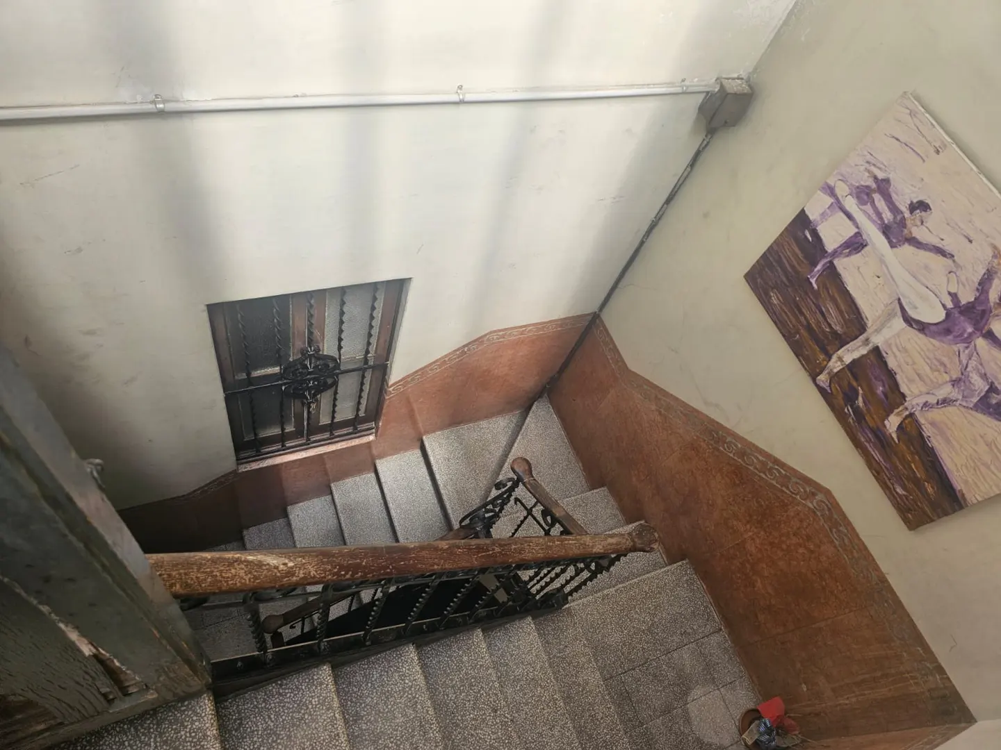 High-angle view of a stone staircase with a wooden handrail, a barred window, and a painting of dancers on the wall.