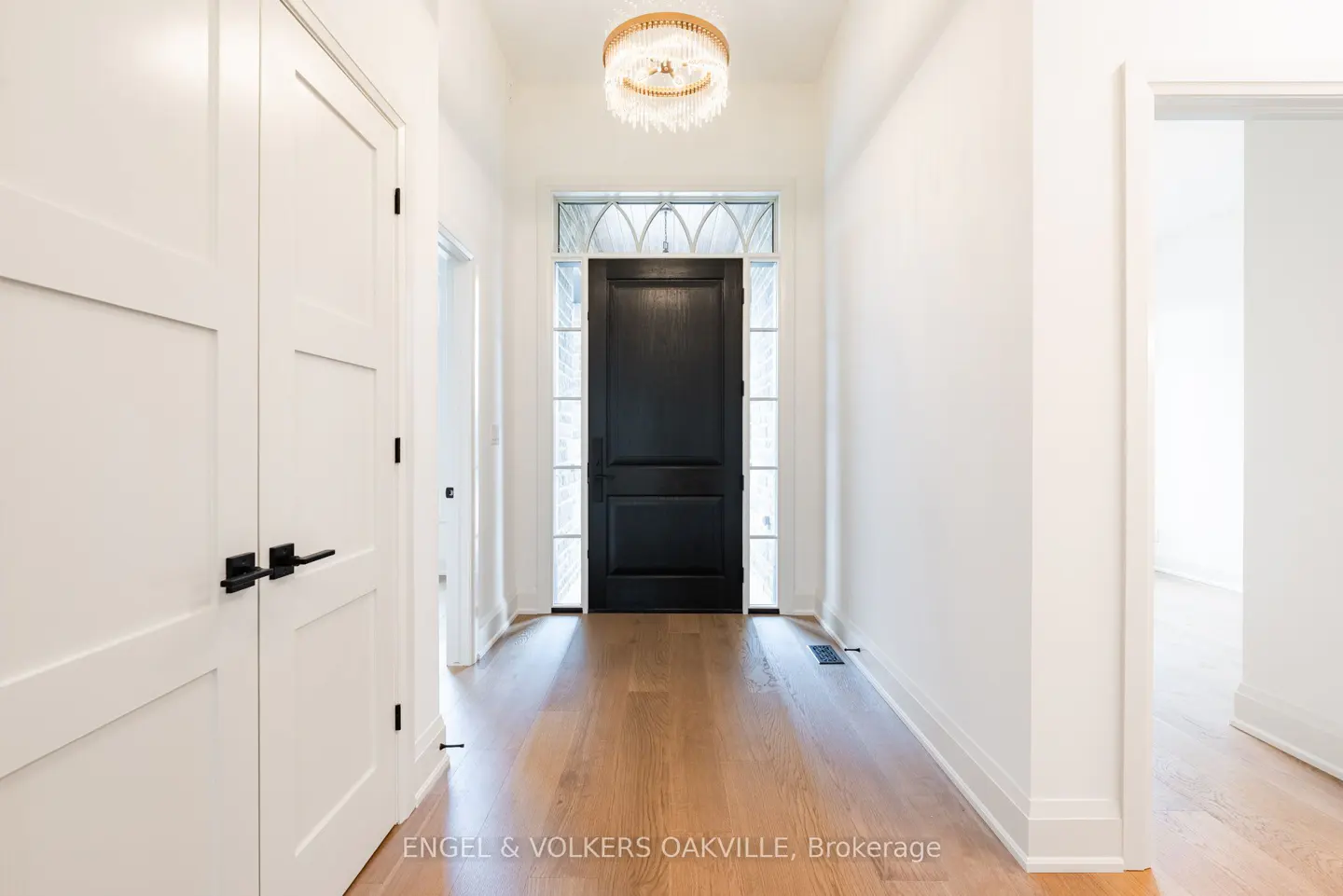 Bright foyer with wood floors, white walls, and a black front door with sidelights. A gold chandelier hangs from the ceiling.