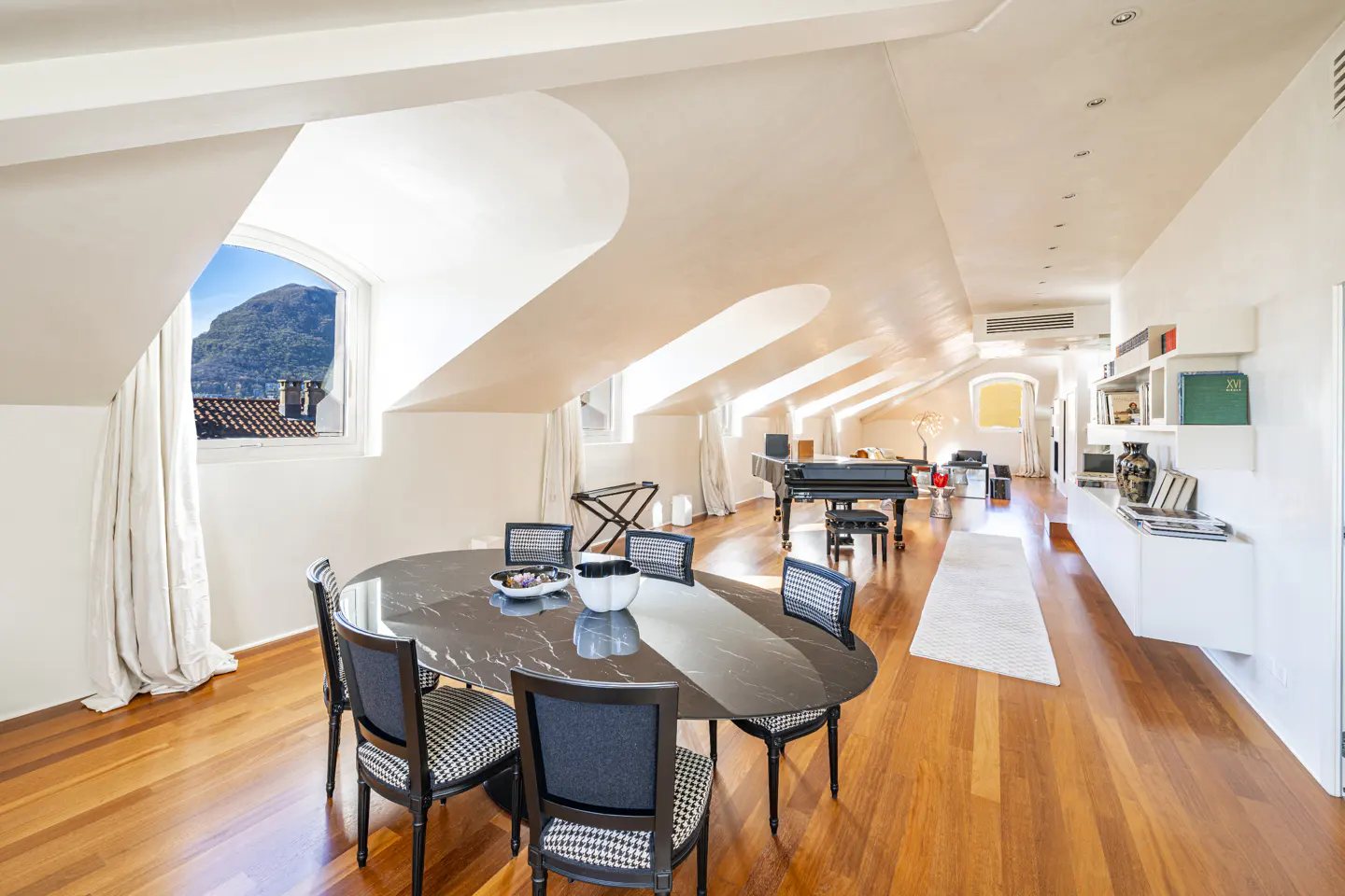 Bright, airy attic apartment with wood floors, oval table, piano, and mountain view.