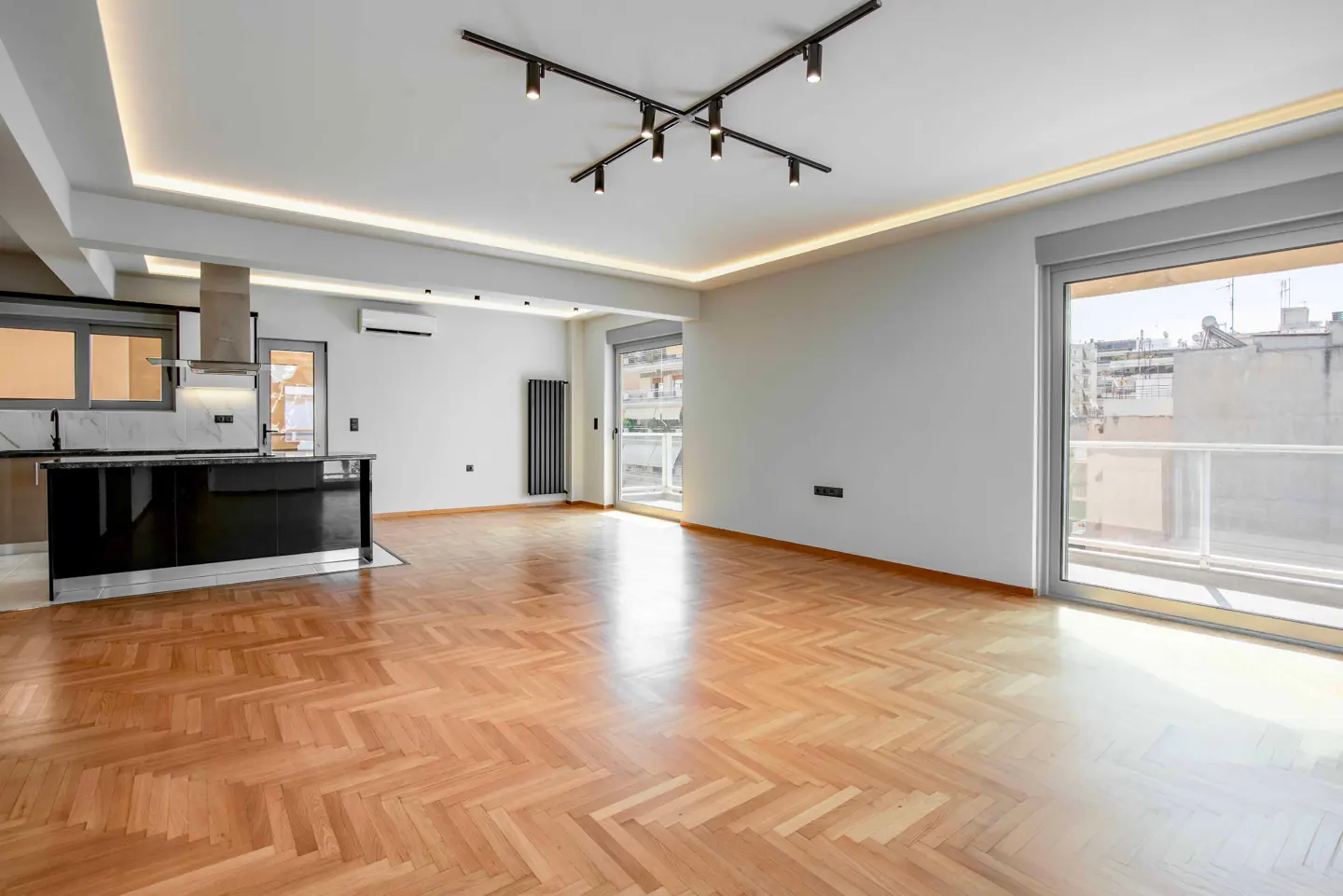 Bright, modern apartment with herringbone wood floors, white walls, and a black kitchen island. Track lighting and large windows.