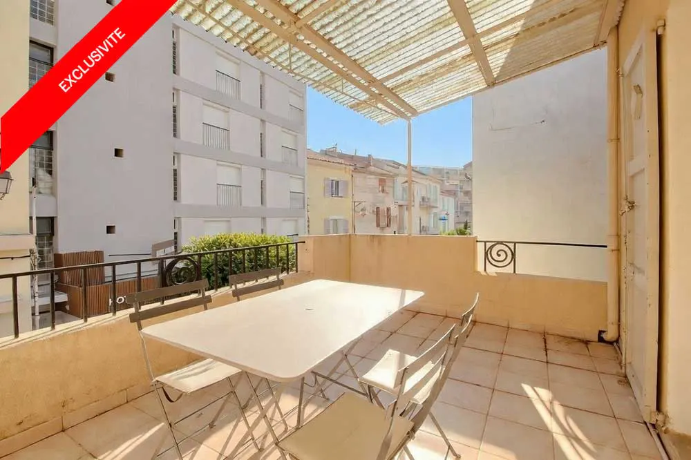 Balcony with a white table and four chairs, a metal awning, and a view of buildings. A red "EXCLUSIVITE" banner is in the corner.