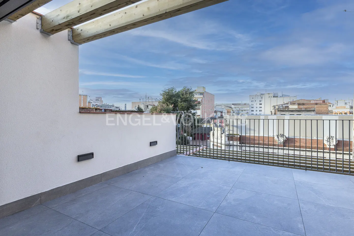 A modern balcony with gray tile flooring and a white wall overlooks a cityscape under a cloudy sky.