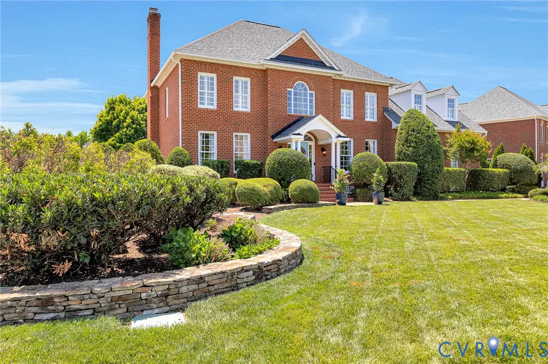 Two-story red brick house with a gray roof, white trim, and a manicured green lawn.