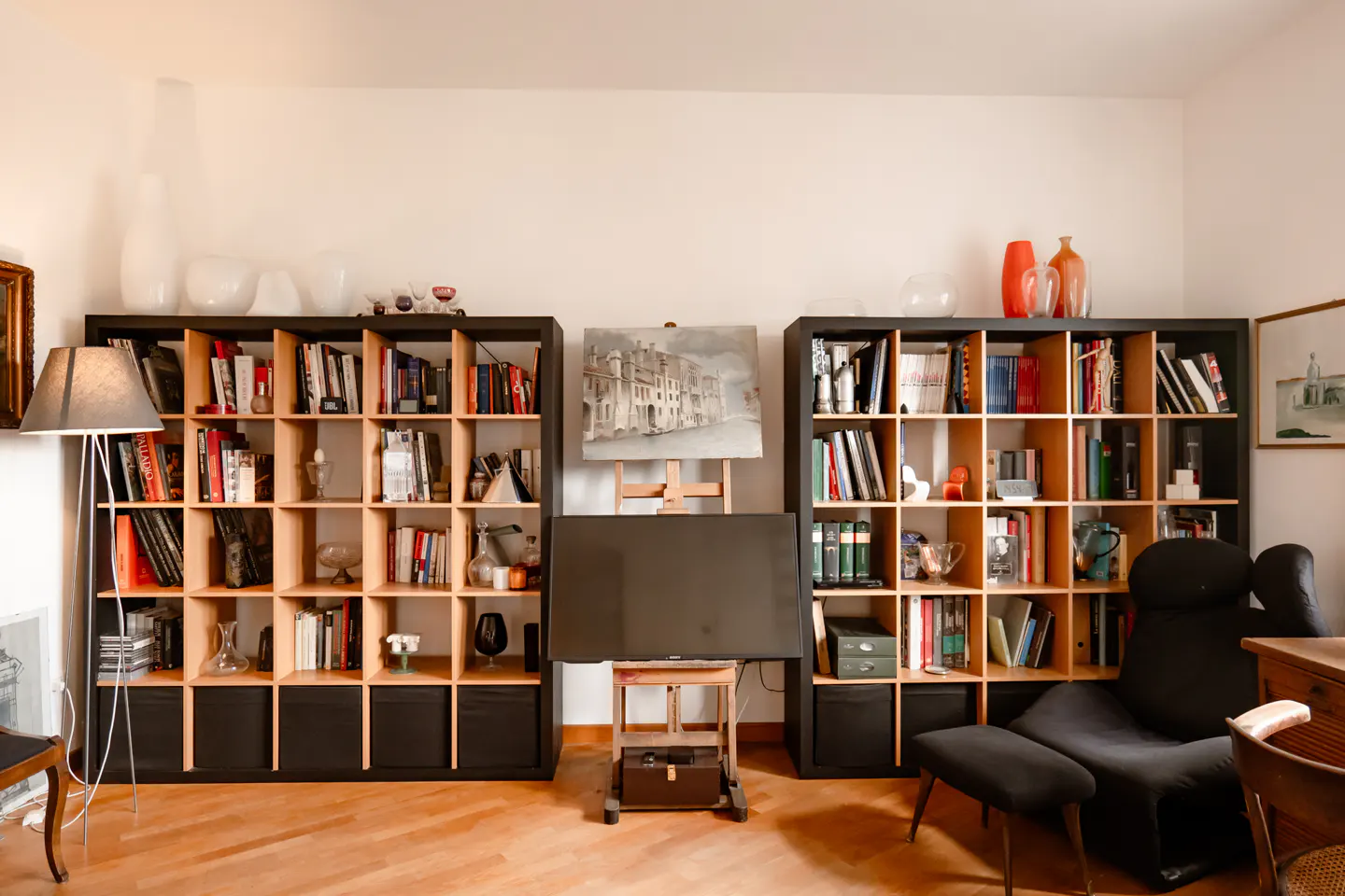 Living room with two black bookshelves filled with books and decor, a painting on an easel, and a black lounge chair.
