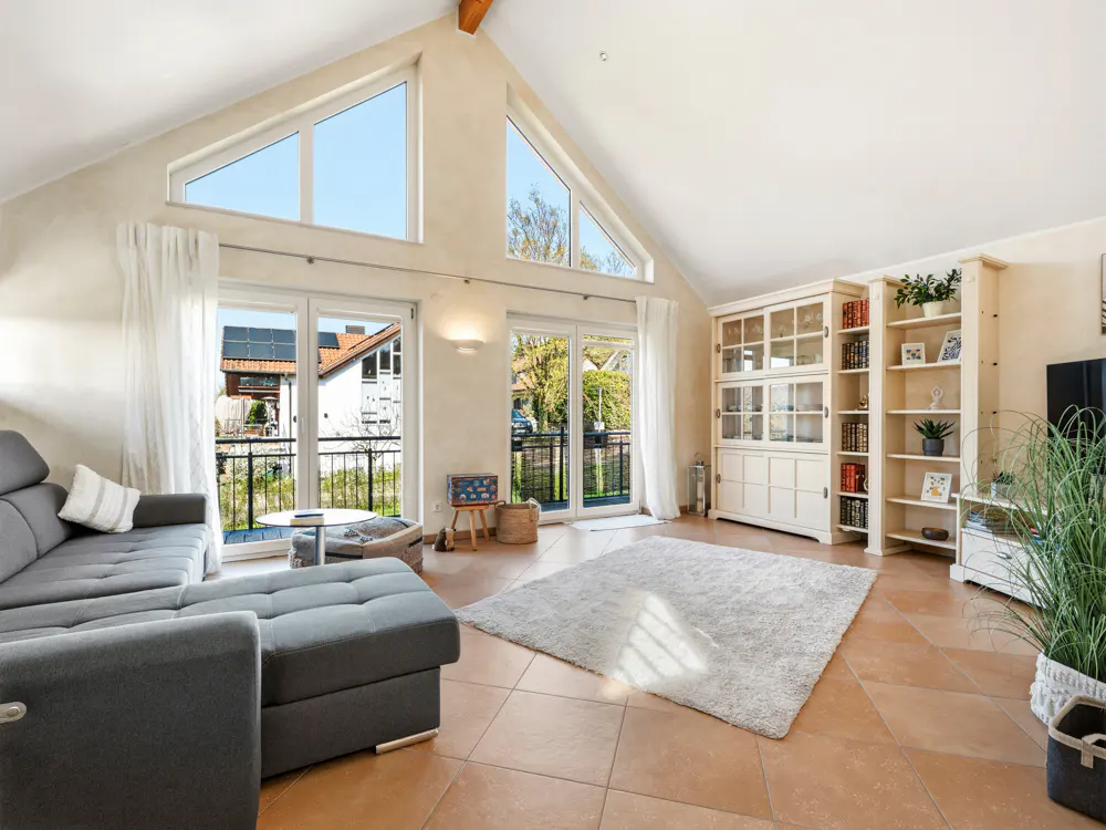 Bright living room with a gray sofa, white rug, and built-in shelves. Large windows offer a view of the outside.