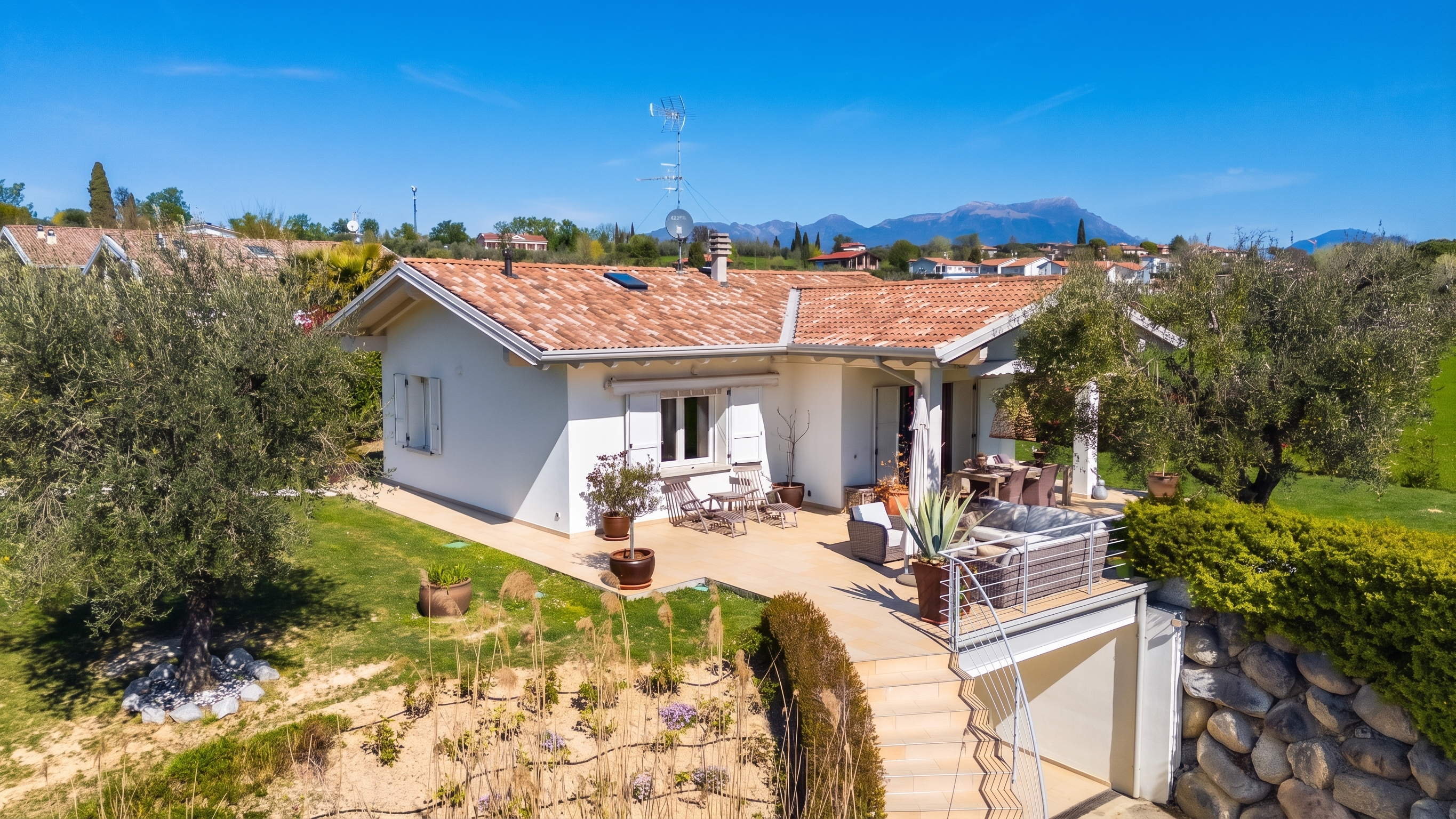 Exterior of a white house with a red tile roof, patio furniture, and a mountain view under a clear blue sky.