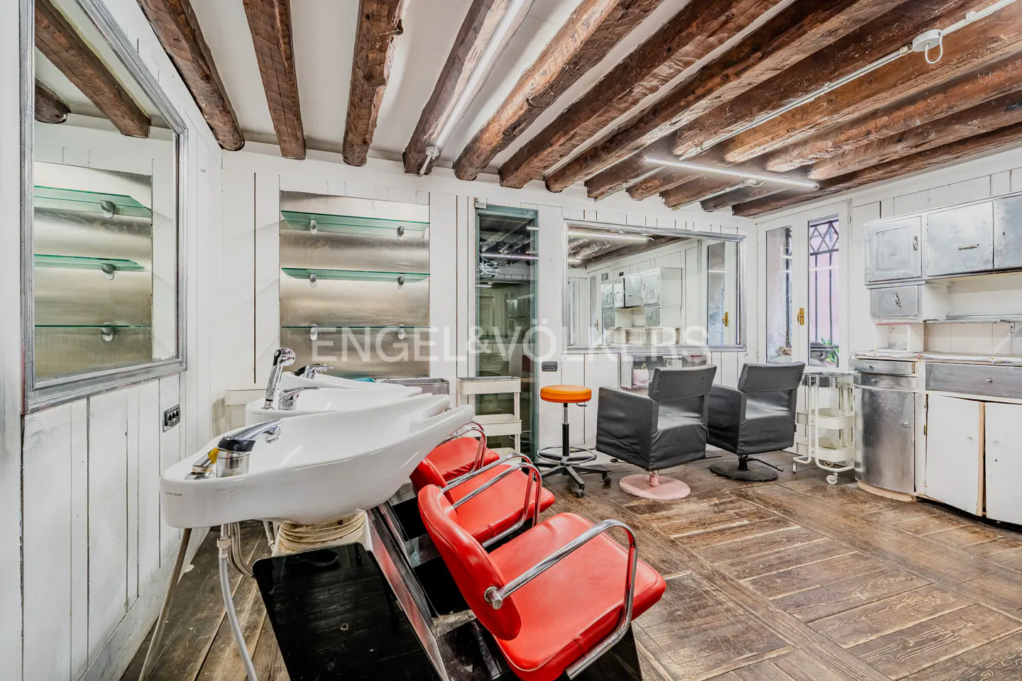 A salon interior with red chairs, white sinks, black styling chairs, and wooden floors and ceiling beams.