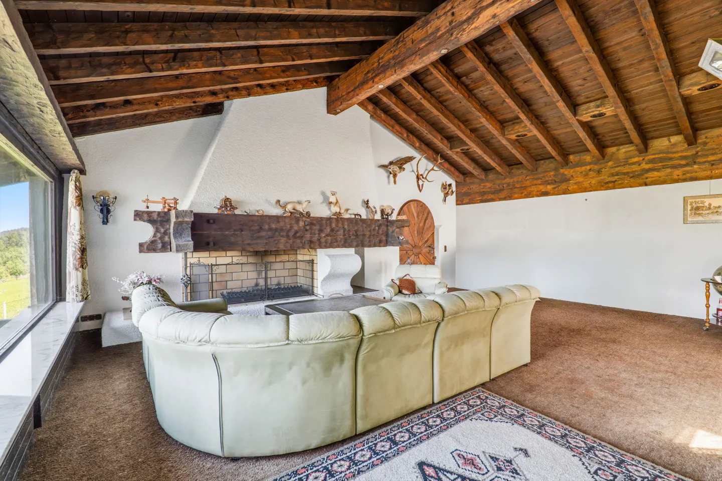 Living room with a light green sofa, brown carpet, and a fireplace with a wooden mantel. The ceiling has exposed wooden beams.