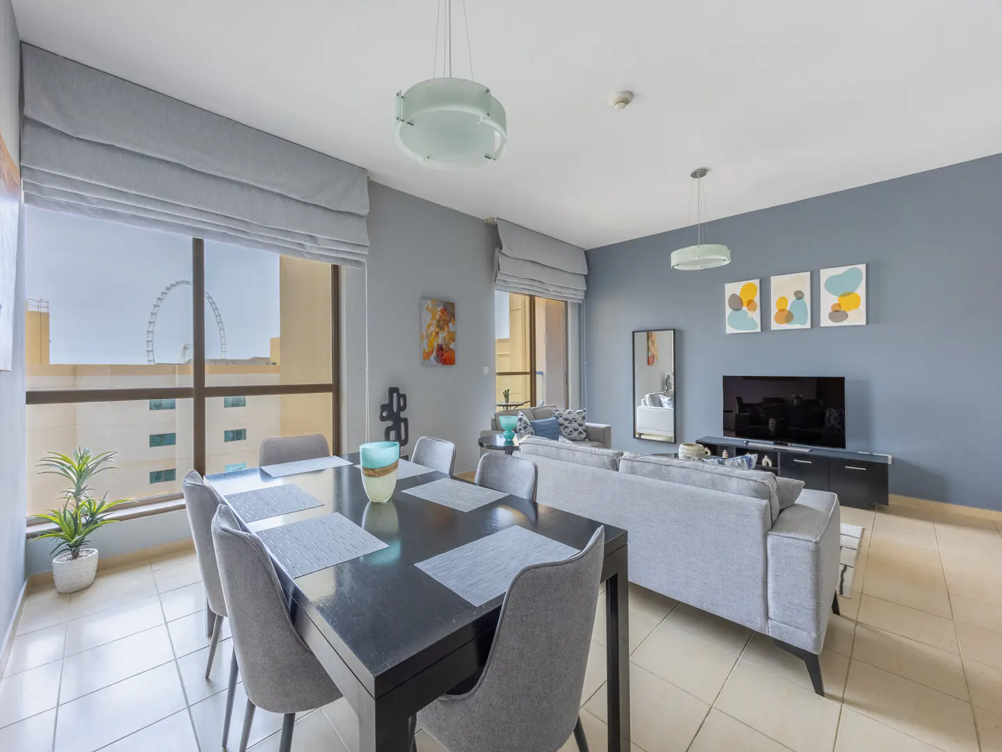 A modern apartment interior with a dining table, gray sofa, and a view of a Ferris wheel.