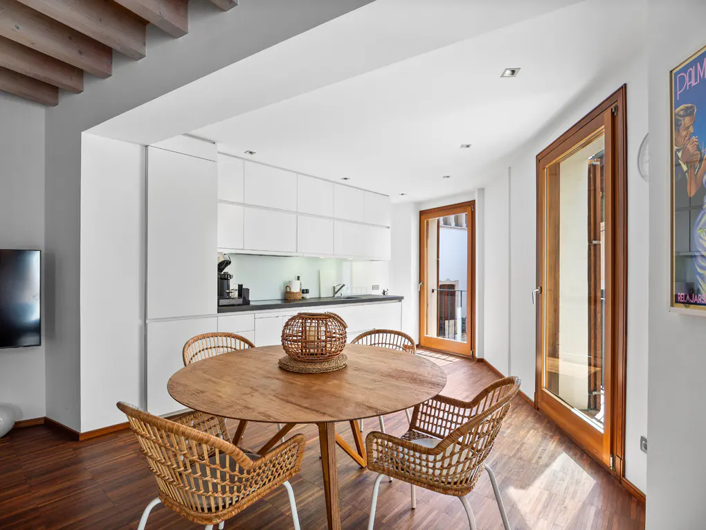 Bright, modern kitchen and dining area with wood floors. A round wood table with four wicker chairs sits in front of white cabinets.