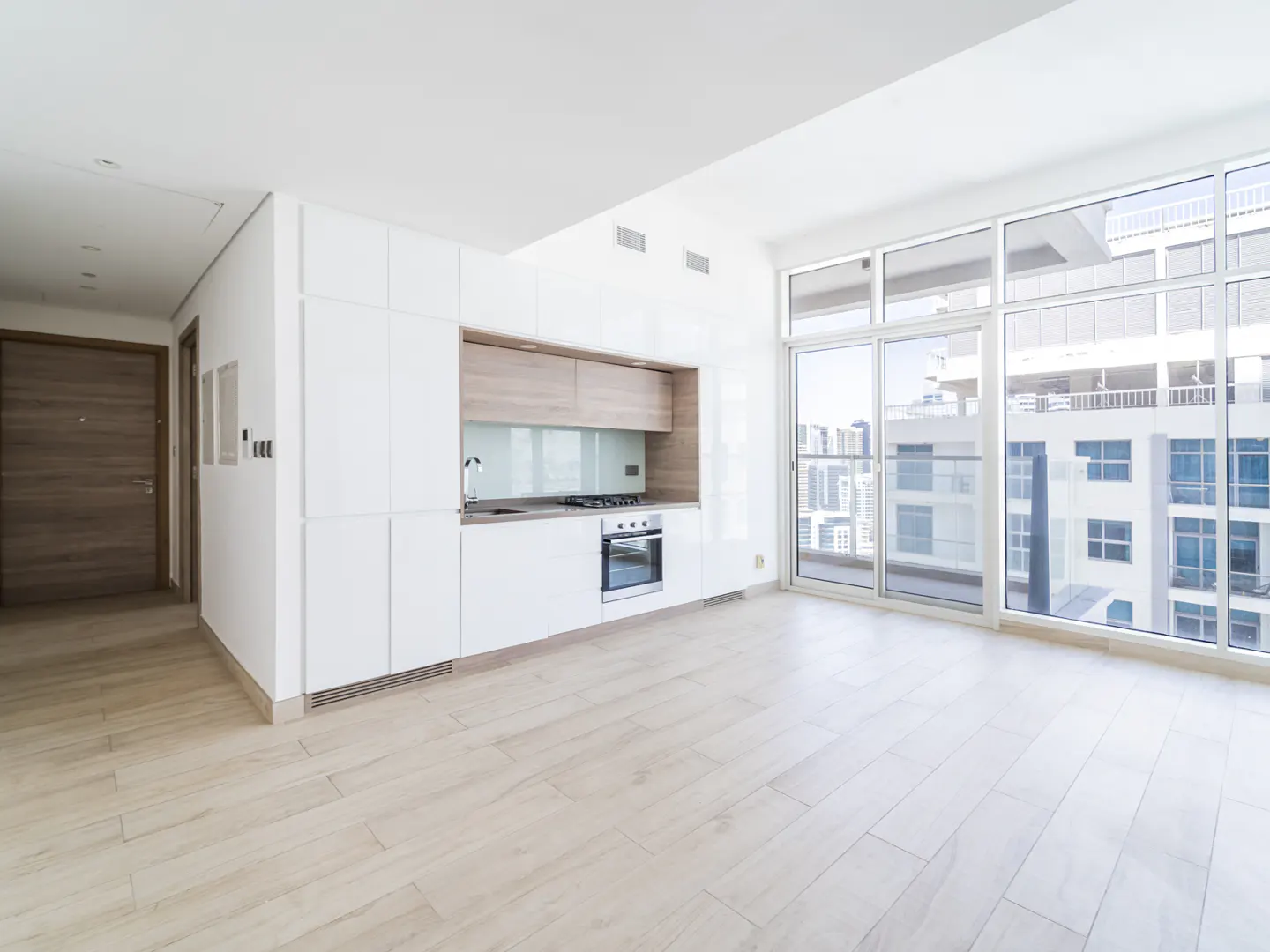 Bright, modern apartment with white cabinets, wood accents, and large windows overlooking a city skyline.