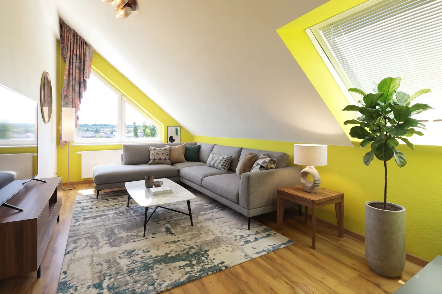 Attic living room with bright yellow walls, a grey sectional sofa, marble coffee table, and a large potted fiddle leaf fig.