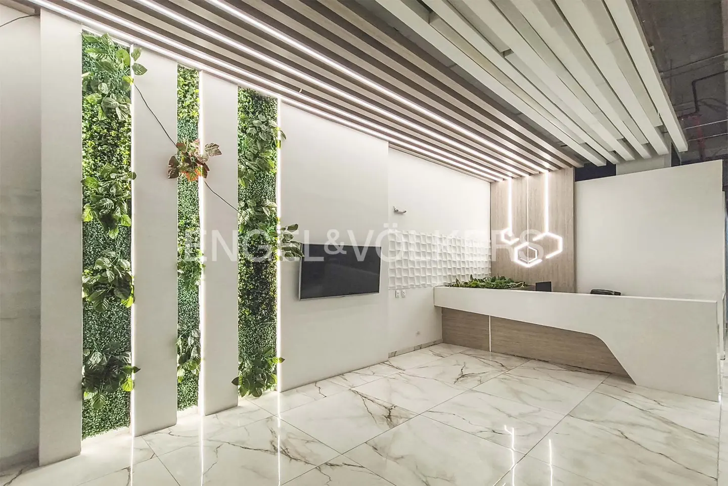 Office lobby with marble floors, a white reception desk, and vertical green walls. A TV hangs on the wall.