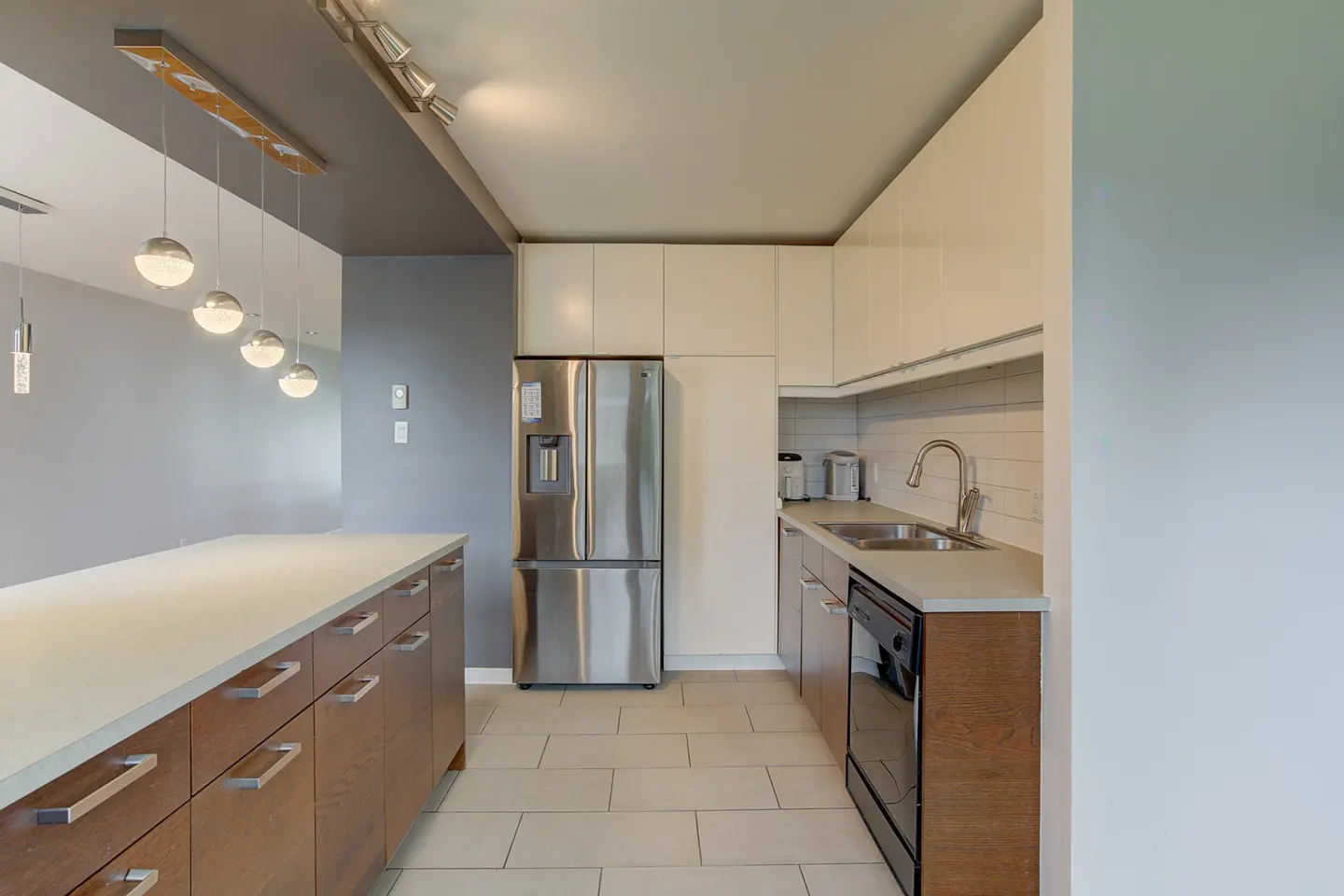 Modern kitchen with white cabinets, stainless steel fridge, wood island, and globe pendant lights.