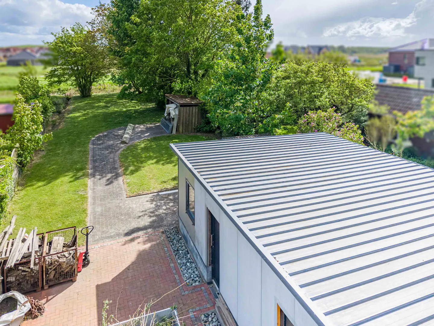 Aerial view of a backyard with a modern shed featuring a striped metal roof, green lawn, and brick patio.