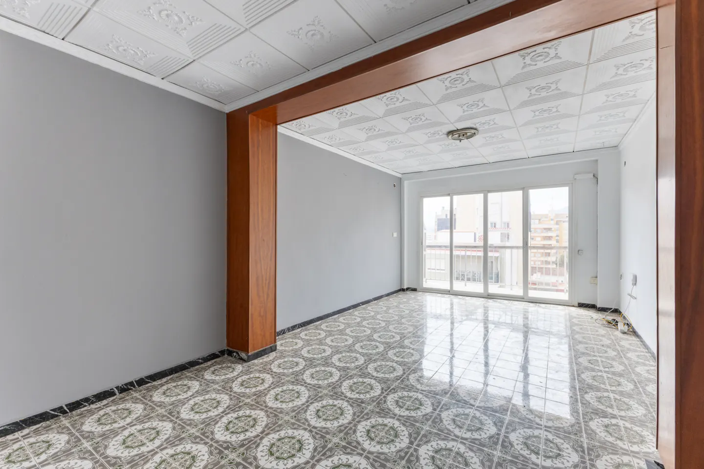 Empty room with gray walls, patterned tile floor, and sliding glass doors to a balcony. Brown wood trim accents the ceiling.