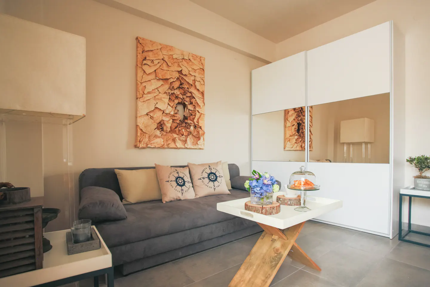 Modern living room with a grey sofa, nautical pillows, a wooden coffee table, and a large white mirrored wardrobe.