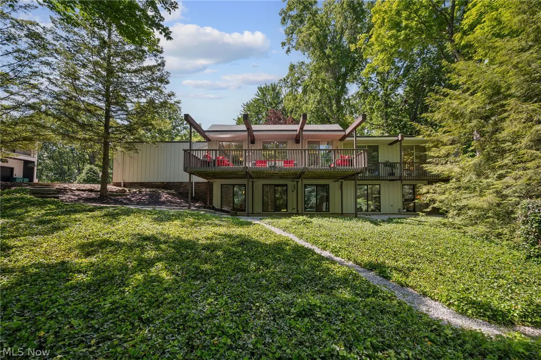 Modern home with a large wooden deck, red patio furniture, and a lush, ivy-covered backyard surrounded by tall trees.