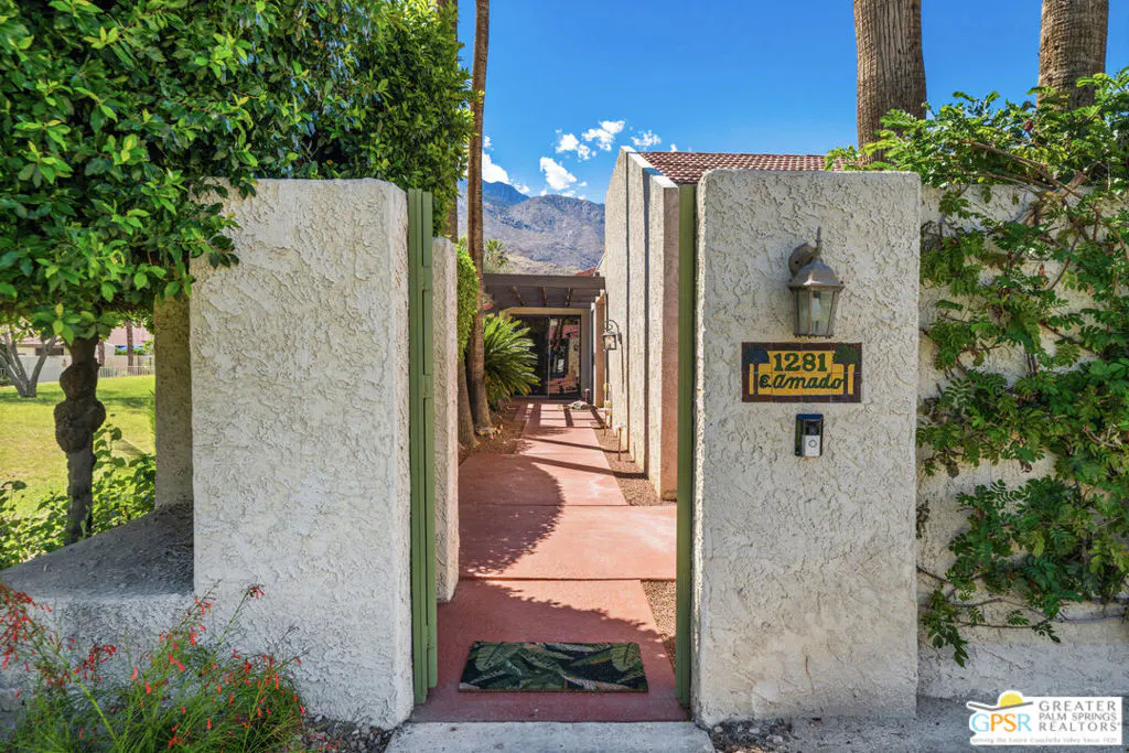View of a home's entrance with stucco walls, a red walkway, and a mountain backdrop under a blue sky. Address plaque reads "1281 E. Amado."