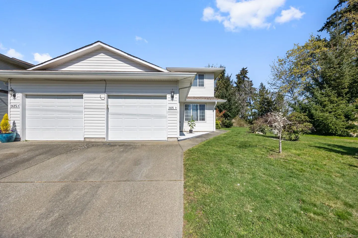 Exterior of a two-story white townhouse with two garage doors, a concrete driveway, and a green lawn.