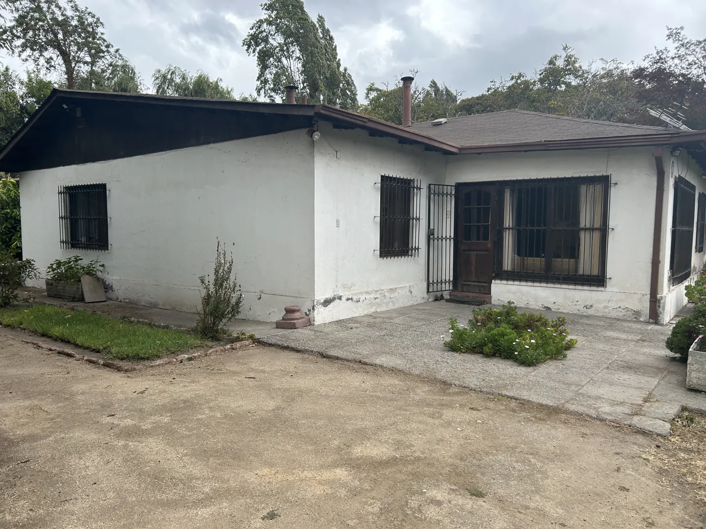 Exterior view of a one-story white house with brown trim and bars on the windows.