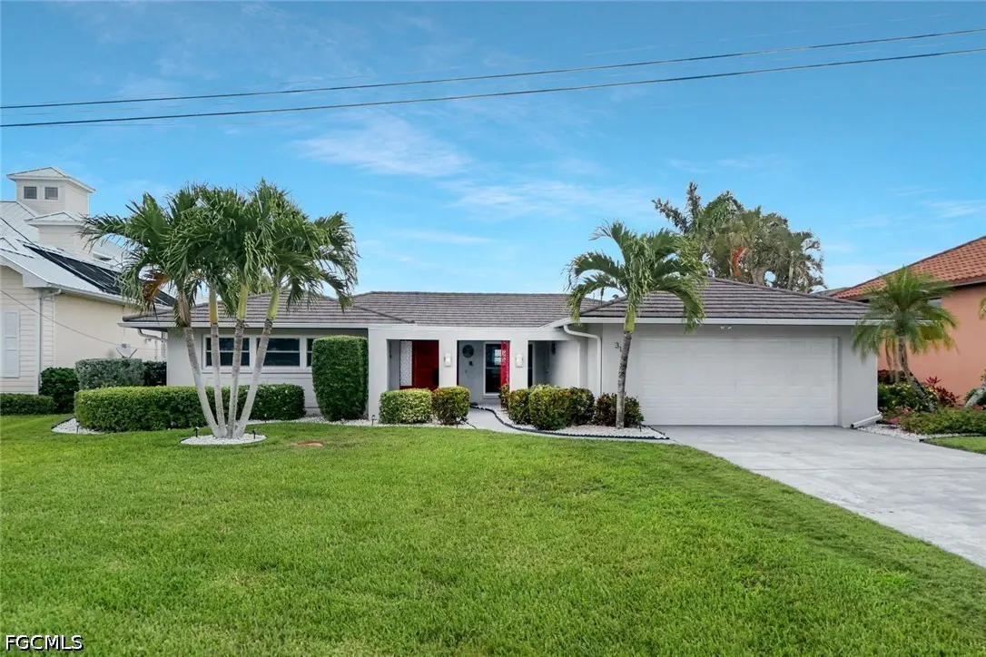 A white, single-story home with a gray roof, red doors, palm trees, and a green lawn.
