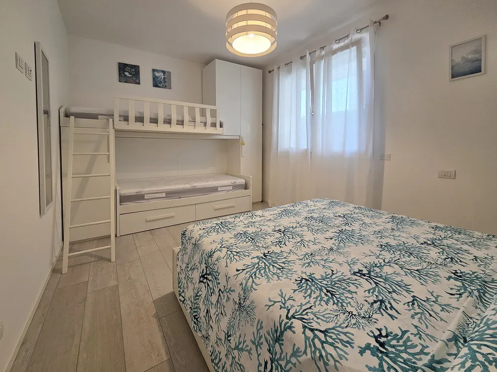 A bright bedroom with a bunk bed, a double bed with a blue coral pattern, and white walls.