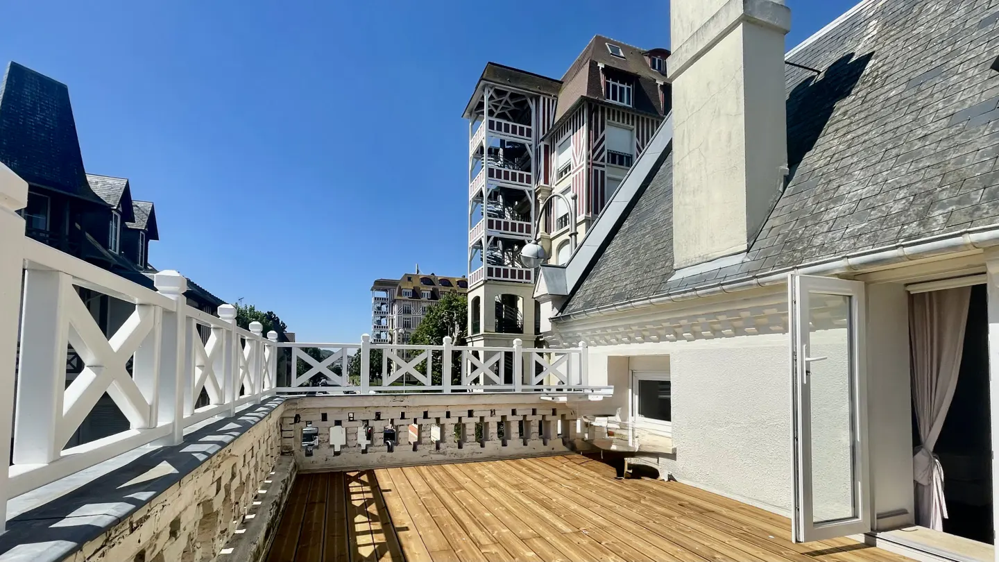 Balcony view with wooden floor, white railings, and a view of buildings under a clear blue sky.