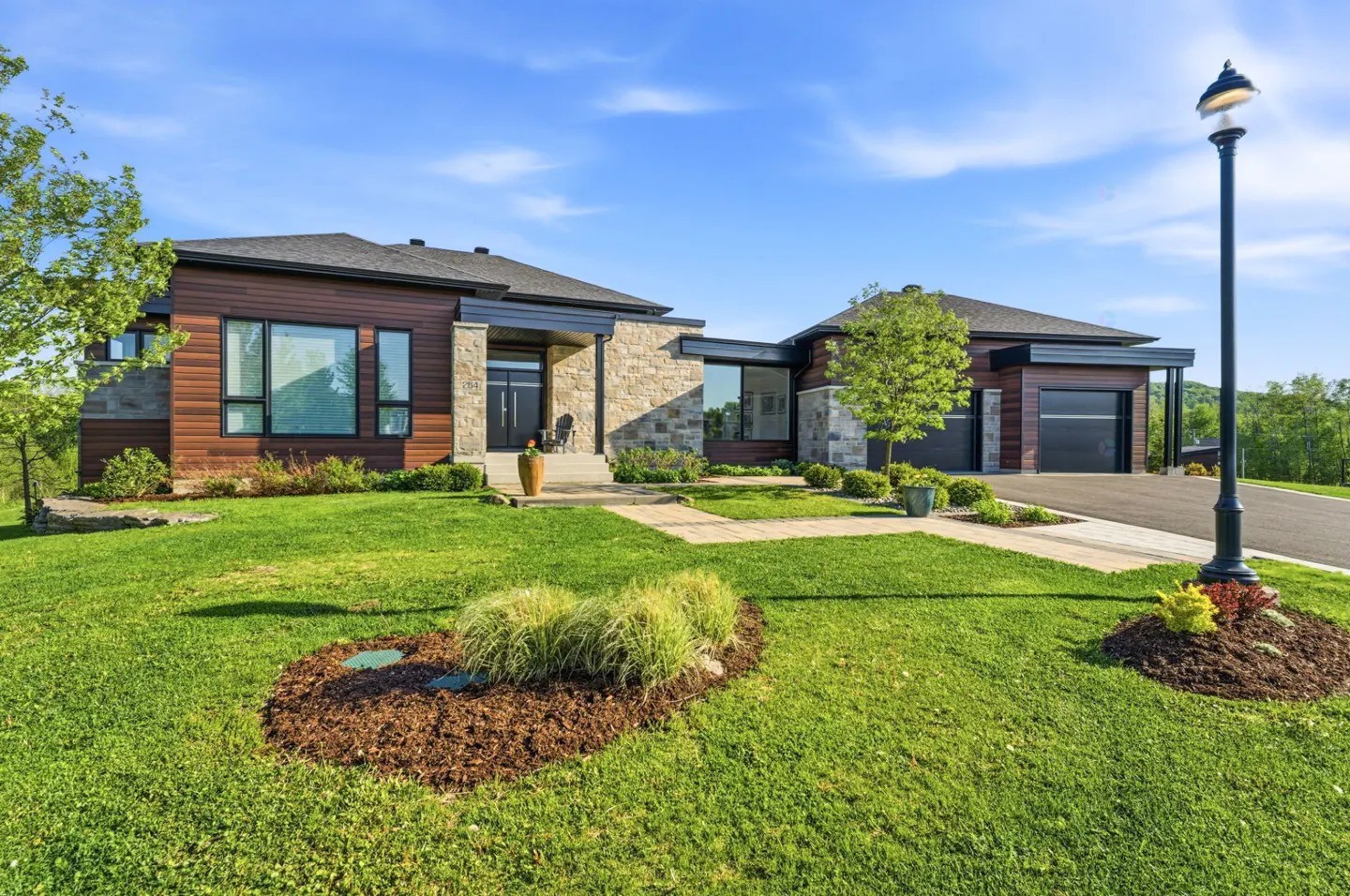 Modern home with wood and stone exterior, green lawn, and blue sky. A lamp post stands to the right.