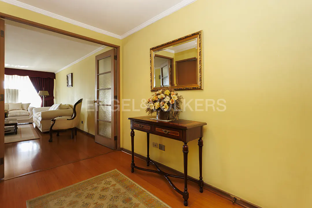 Entryway with wood floors, yellow walls, and a gold-framed mirror above a dark wood console table with flowers. Living room visible through doorway.