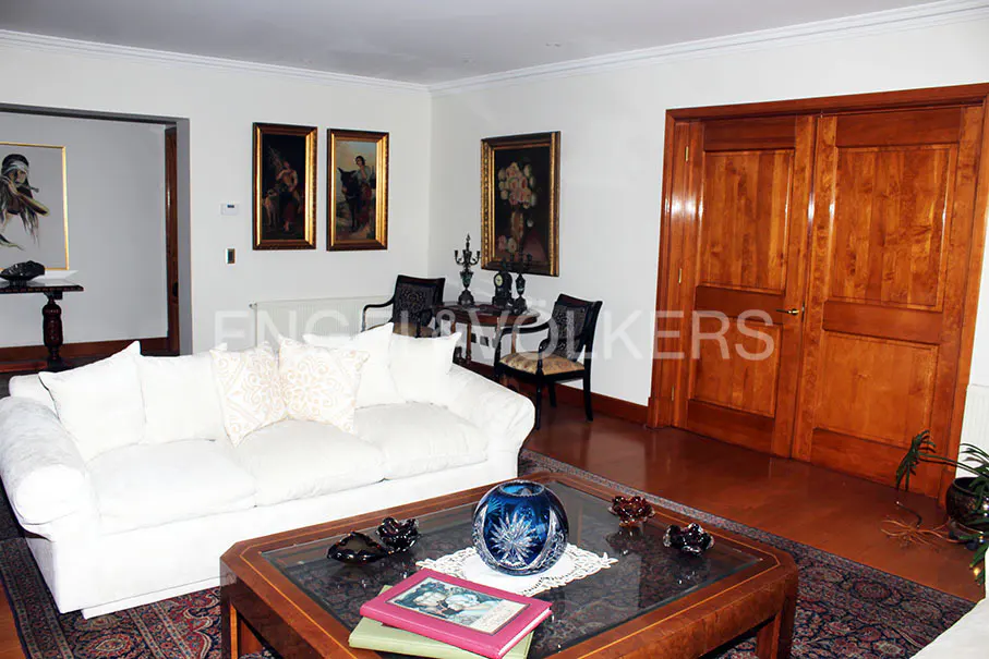 Living room with a white sofa, wood floors, and a glass-topped coffee table on a patterned rug. Paintings adorn the walls.