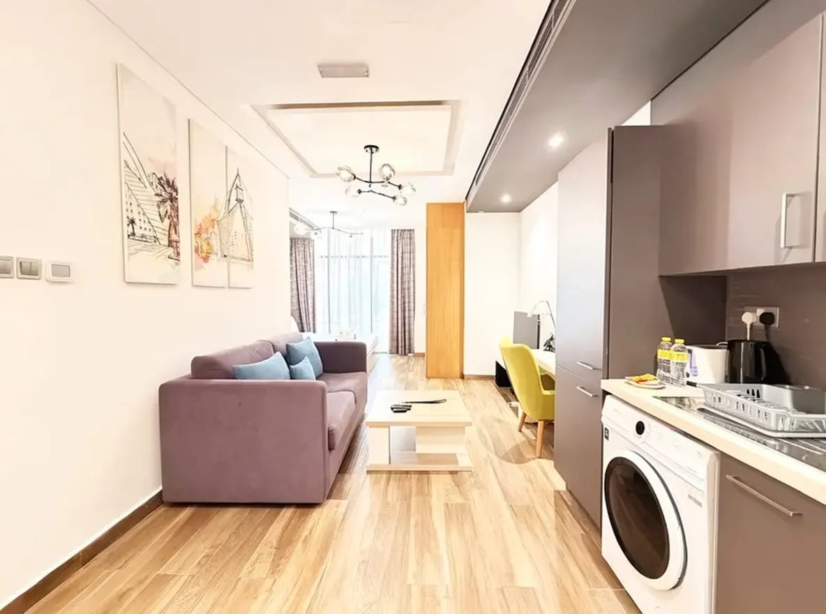 A modern apartment interior with a purple sofa, light wood floors, and a kitchen area with gray cabinets.