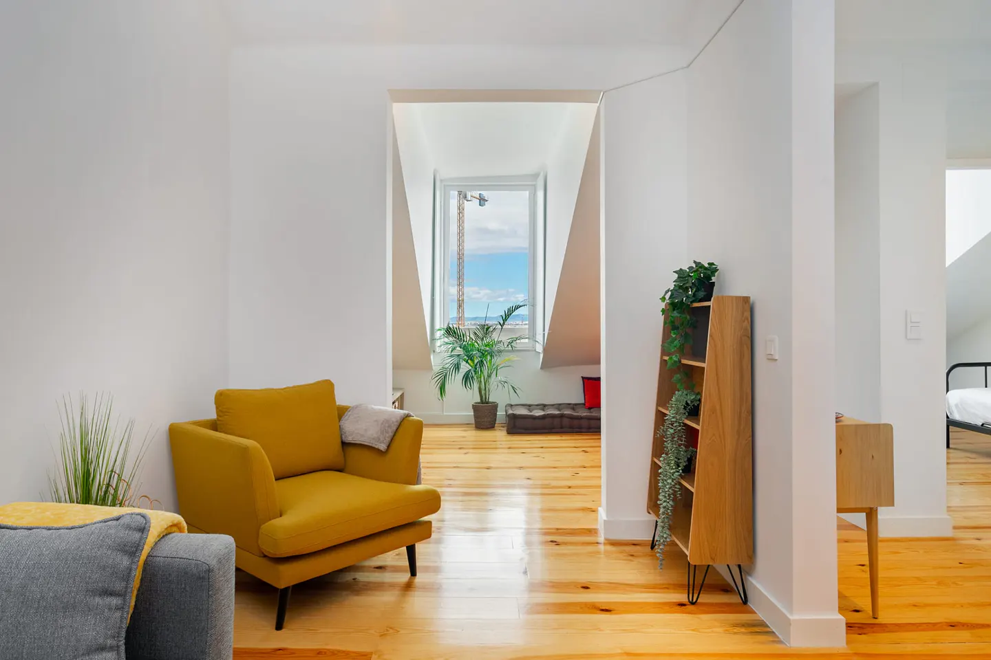 Bright, modern living room with hardwood floors, white walls, and a yellow armchair. A window shows a cityscape in the background.