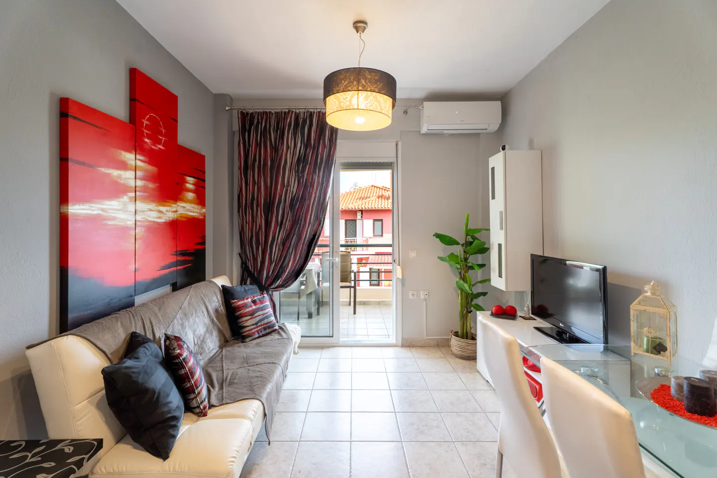 Living room with a white sofa, red artwork, and a balcony view. The walls are gray, and a modern light fixture hangs from the ceiling.