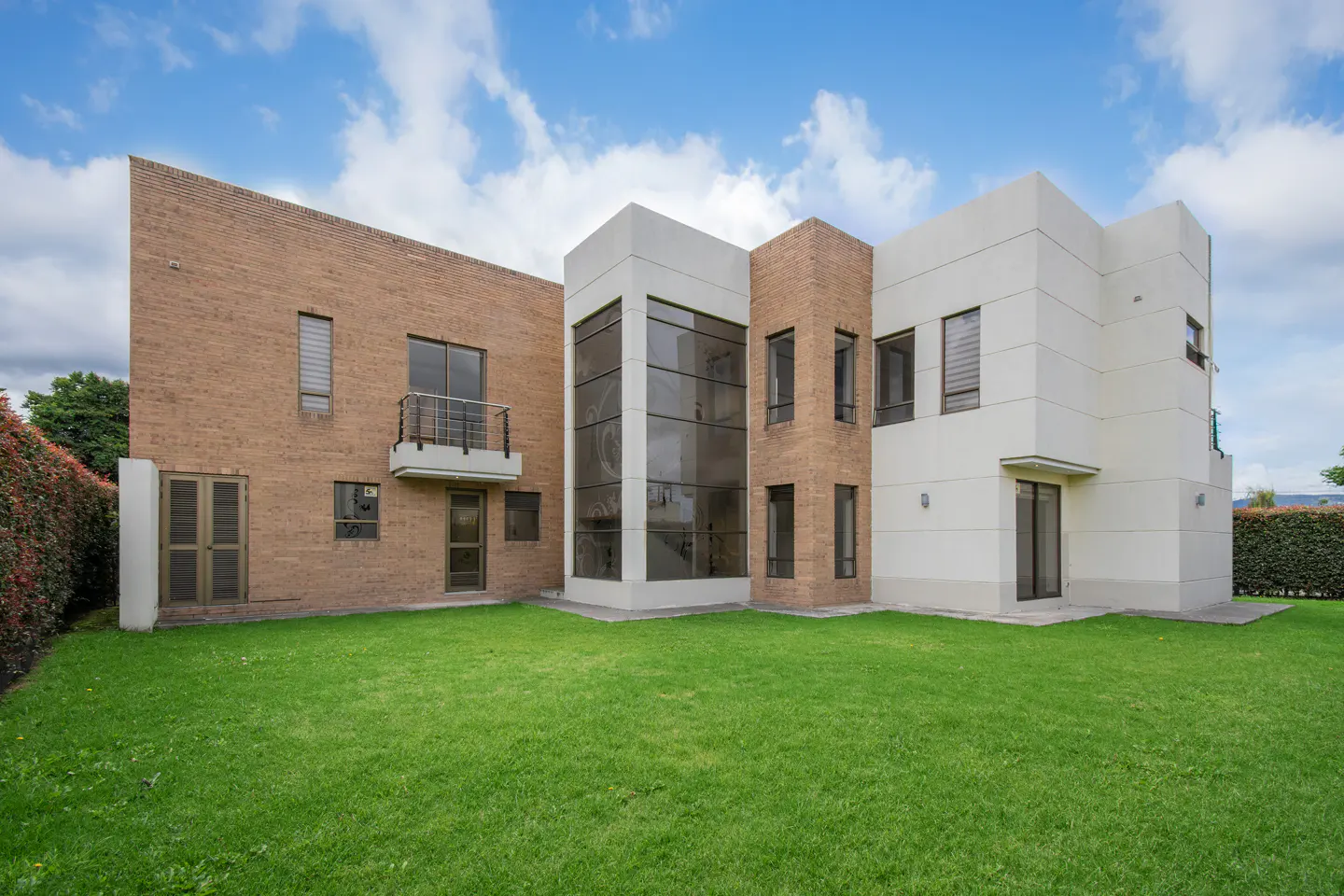 Modern two-story house with brick and white facade, large windows, and green lawn under a blue sky.