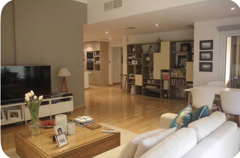 Open-plan living room with white sofa, wooden coffee table, TV, and a large shelving unit leading to a modern kitchen.