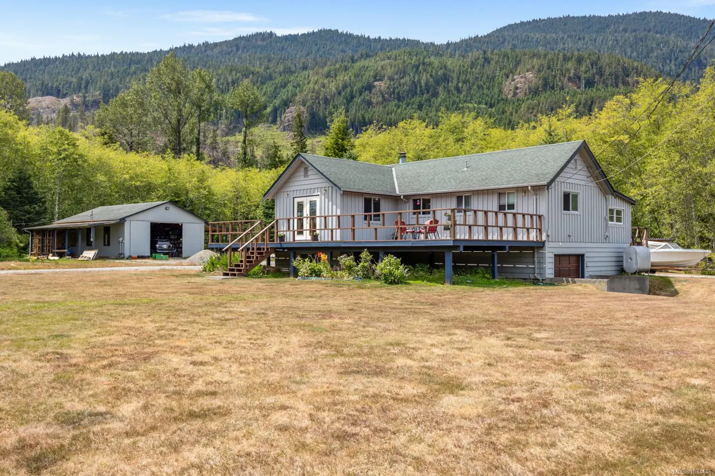 Exterior of a light gray house with a green roof and a large deck, with a mountain backdrop.