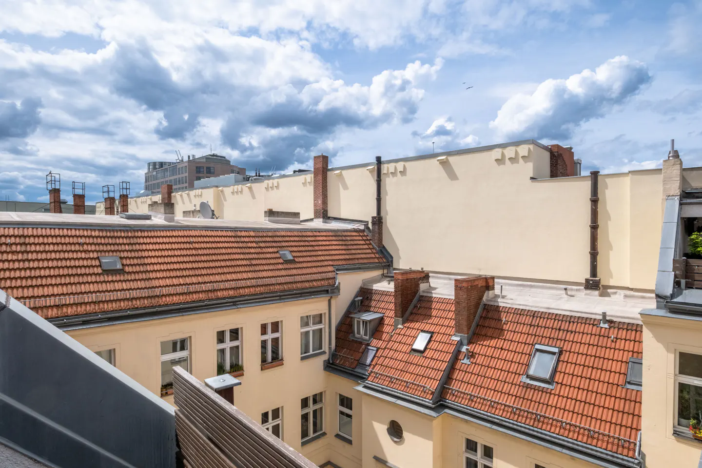 High-angle view of cream-colored apartment buildings with red-tiled roofs under a cloudy blue sky.