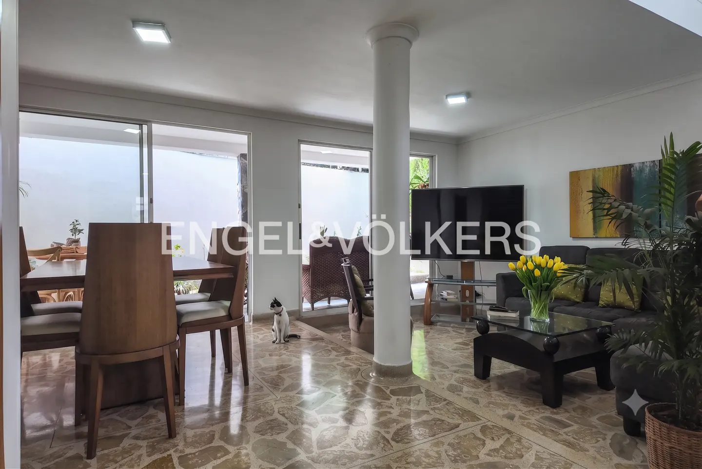 Open-concept living and dining area with stone floors, a central pillar, a dining set, a sofa, and a cat on the floor.