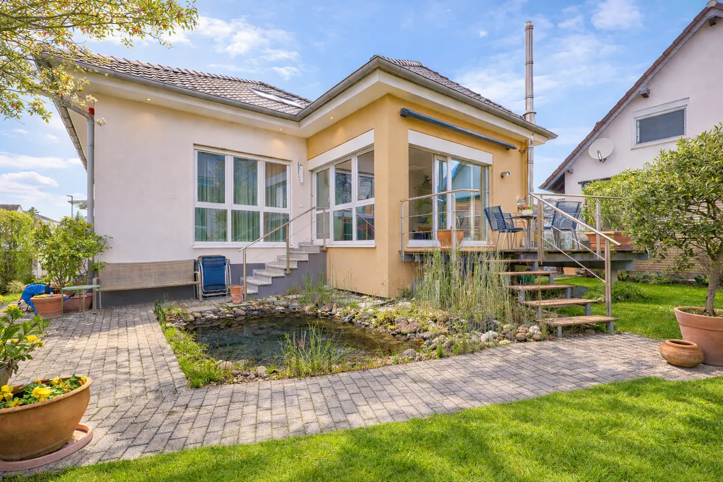 Backyard view of a cream and yellow house with a pond, patio, and green lawn.