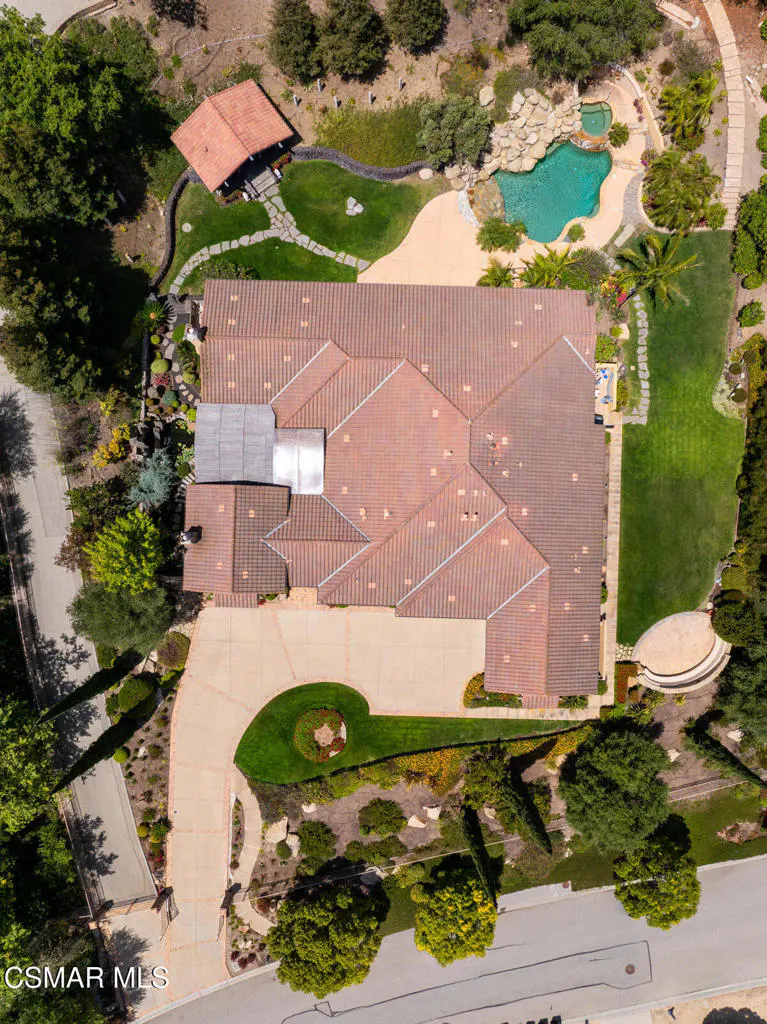 Aerial view of a home with a brown tile roof, a curved driveway, a swimming pool, and lush landscaping on a large lot.